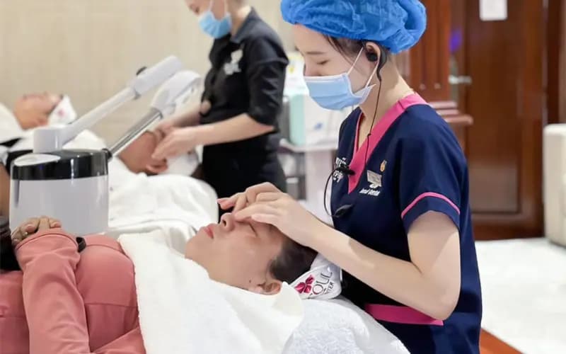 Kỹ thuật viên massage da mặt, khách nằm thư giãn